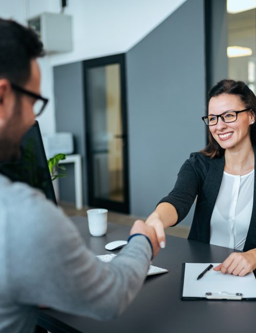 Businesswoman and businessman shaking hands in modern office.