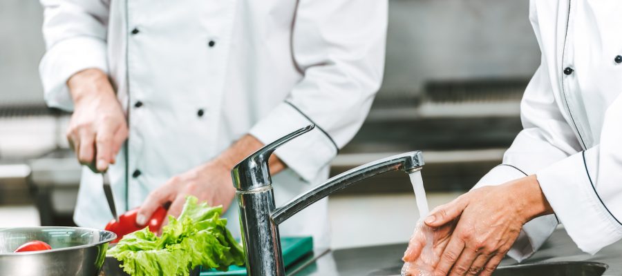 cropped view of female chef washing hands over sink while colleague cooking on background in restaurant kitchen