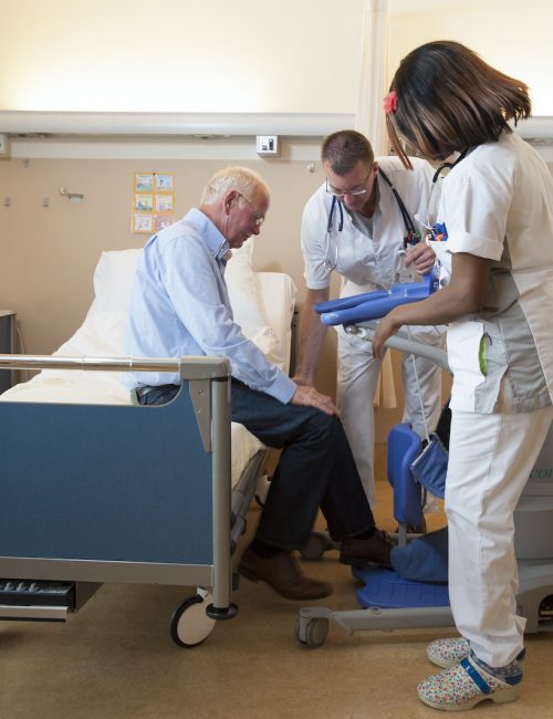 Verpleegkundigen helpen een patient uit bed met een til lift. Nurses helping a patient out of bed with a active lifter.